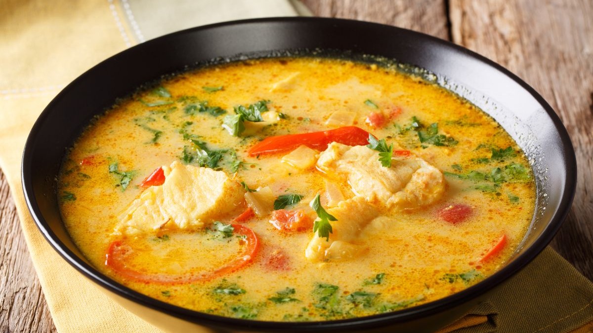 A cremosidade da moqueca baiana, com peixe, pimentões e coentro, é ideal para aquecer o corpo nos dias mais frescos em Salvador. Moqueca de peixe cremosa em tigela preta com pimentão vermelho e coentro.