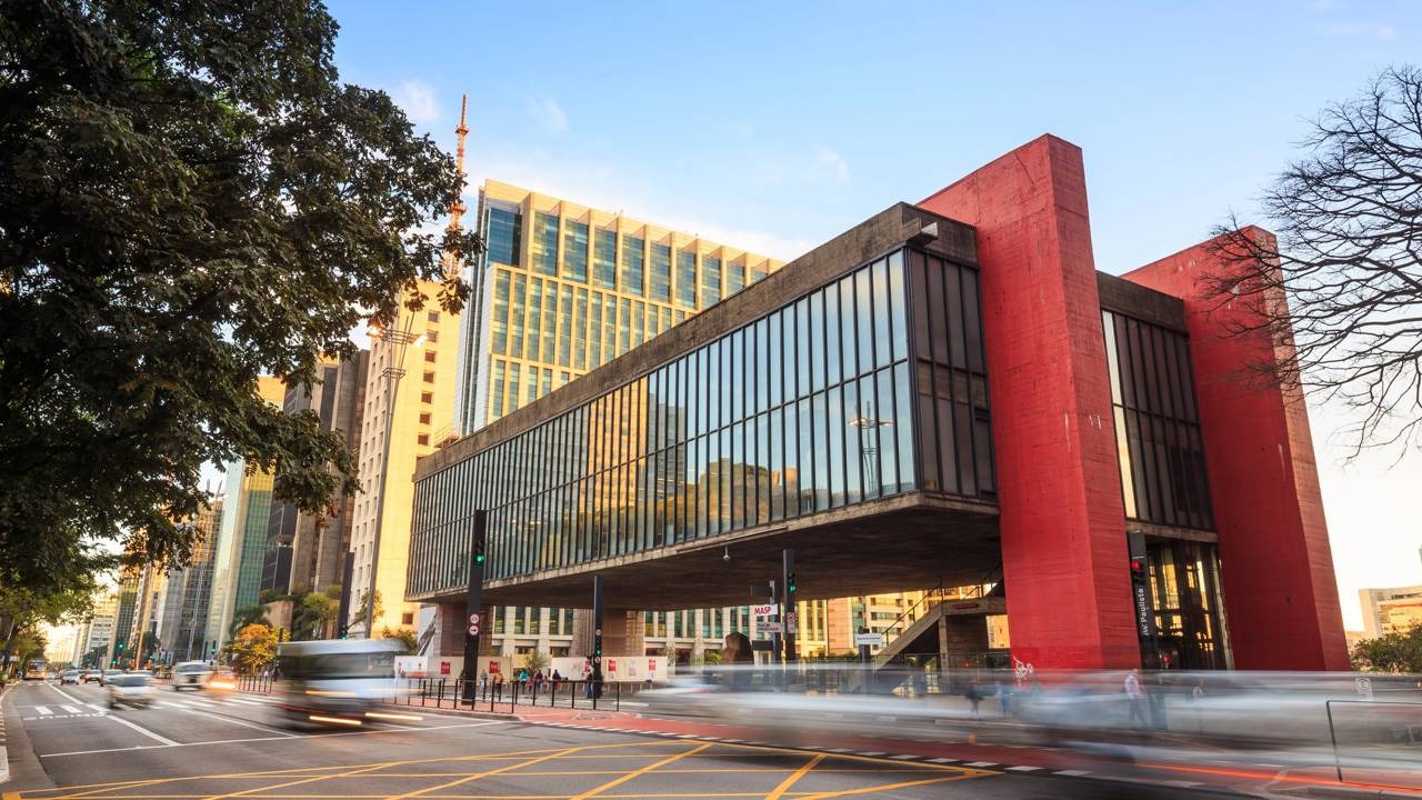 O MASP, na Avenida Paulista, é um dos pontos turísticos icônicos no roteiro de 48 horas pela capital paulista. Vista externa do MASP, edifício vermelho e concreto com faixas de vidro, avenida movimentada.