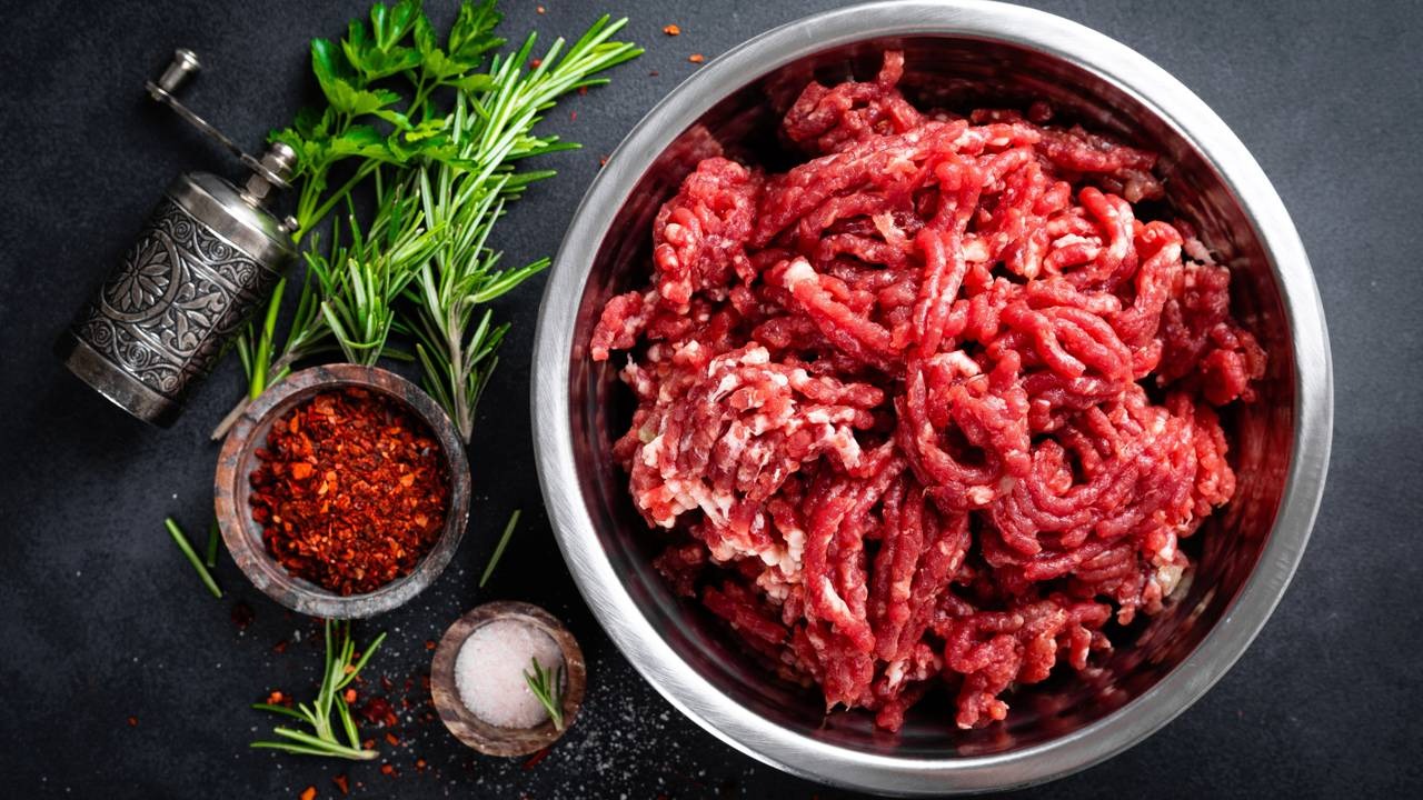 O tipo de carne moída e seus temperos são decisivos para a suculência e textura de hambúrgueres, almôndegas e outros pratos Tigela de carne moída crua com alecrim, salsa, moedor, pimenta e sal grosso