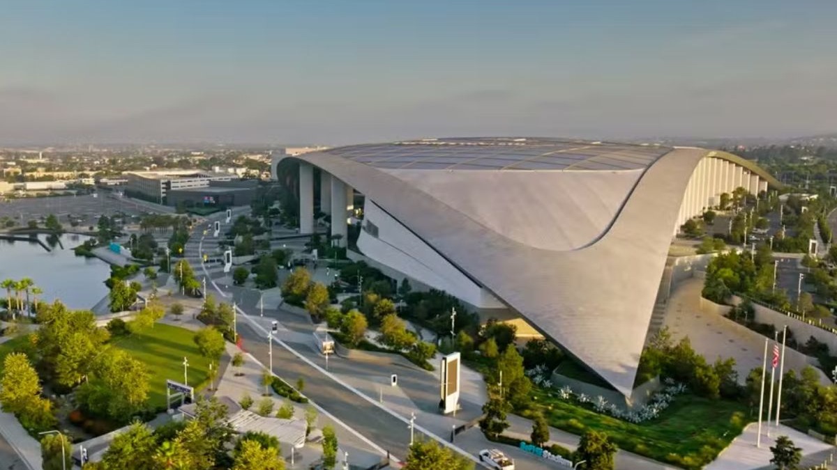 O SoFi Stadium, em Los Angeles, ilustra o design futurista das arenas que sediarão a Copa do Mundo de 2026. Vista aérea do SoFi Stadium, Los Angeles, com teto ondulado, lago e paisagismo.