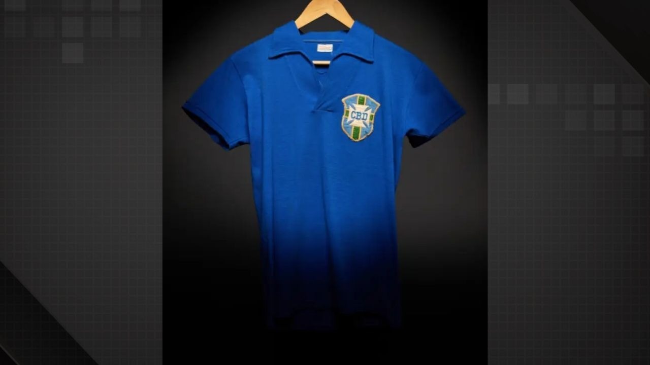 A icônica camisa azul usada por Pelé na final da Copa do Mundo de 1958, leiloada por R$ 25 milhões Foto: Sotheby's/Divulgação Camisa de futebol azul com gola V e distintivo CBD, pendurada em cabide
