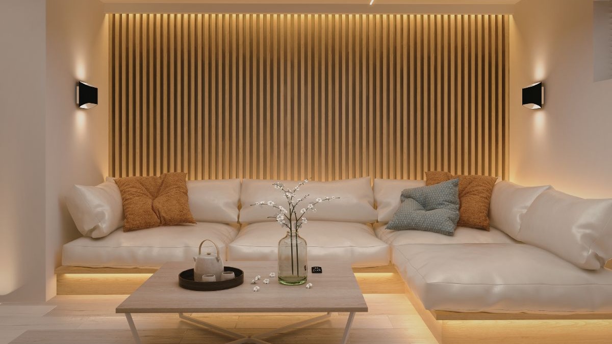 Sala de estar com sof&aacute; secional bege, painel ripado de madeira e ilumina&ccedil;&atilde;o indireta.