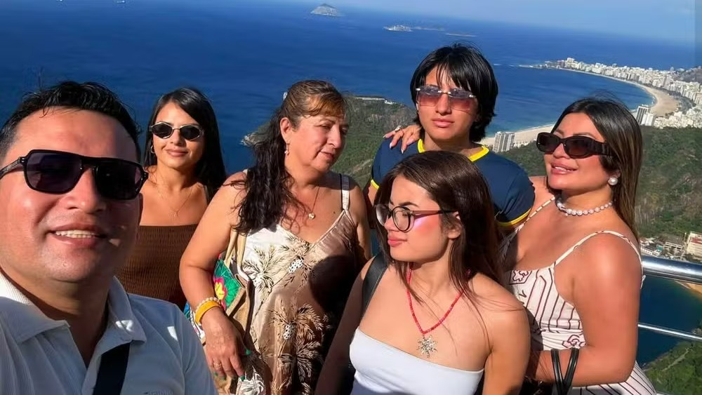Registro da família colombiana durante a viagem ao Rio de Janeiro, antes do trágico acidente de helicóptero. Foto: Reprodução Seis turistas sorrindo em ponto turístico com vista do mar e cidade do Rio