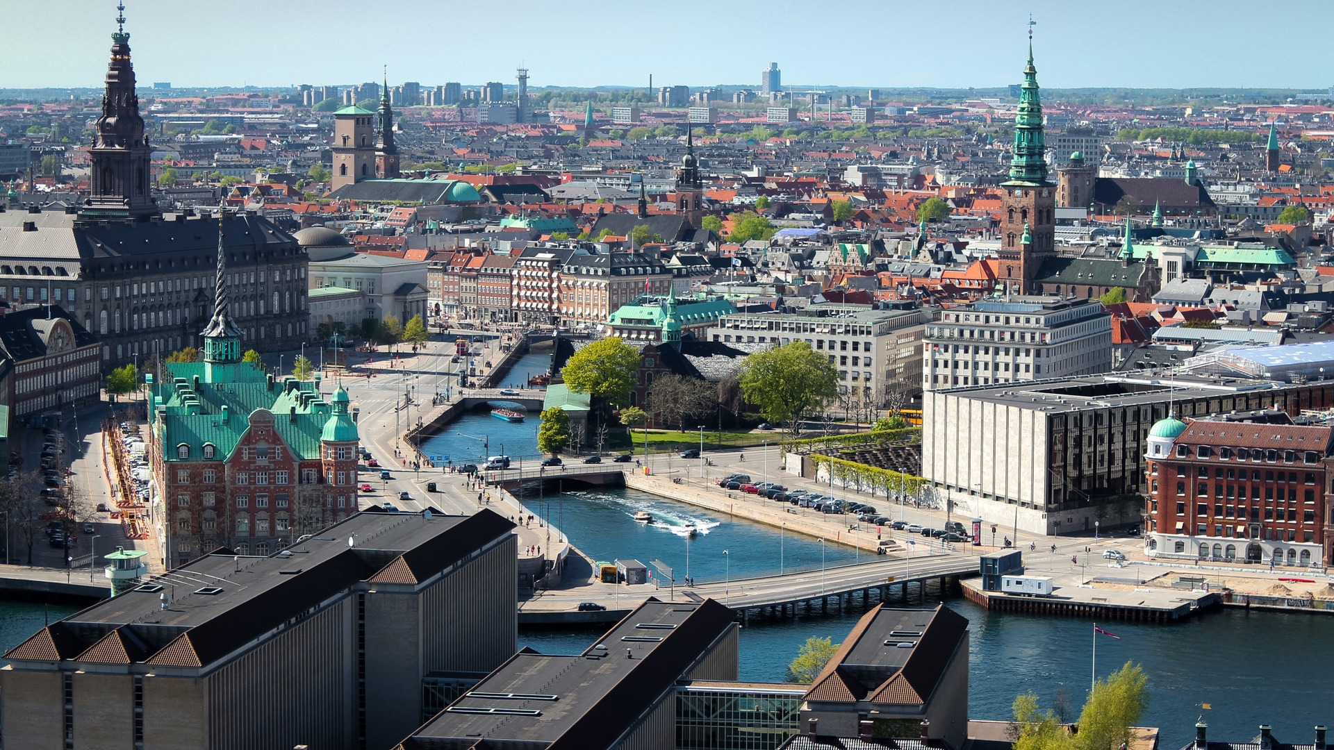 Copenhague, capital dinamarquesa, é reconhecida por sua qualidade de vida e ambiente acolhedor, ideal para jogadores que valorizam bem-estar. Vista aérea de Copenhague com canais, edifícios históricos, telhados verdes e ruas movimentadas.