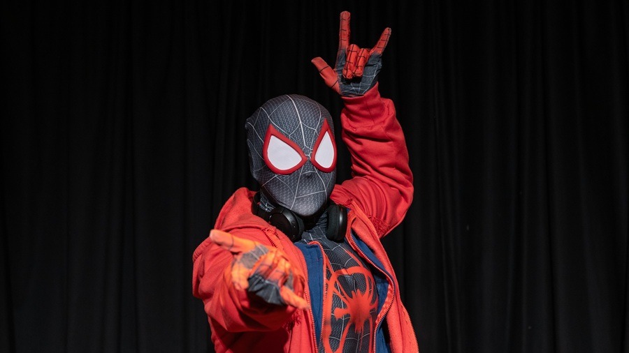 Homem-Aranha Miles Morales em traje preto e vermelho, com fone no pesco&ccedil;o, faz gestos com as m&atilde;os