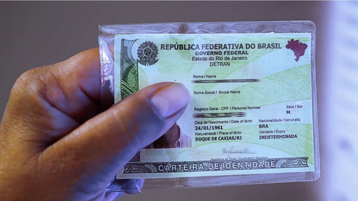 Mão segurando Carteira de Identidade Nacional brasileira com dados parcialmente visíveis e validade indeterminada.