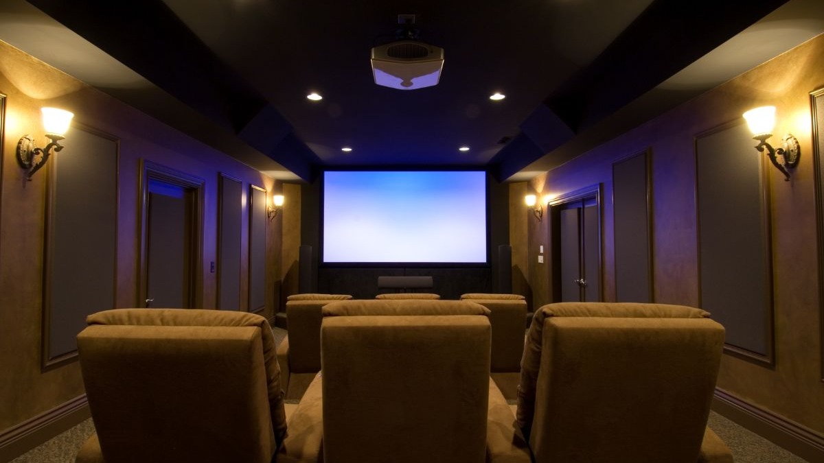 Sala de cinema residencial escura com tela grande, projetor, poltronas reclin&aacute;veis e ilumina&ccedil;&atilde;o ambiente.