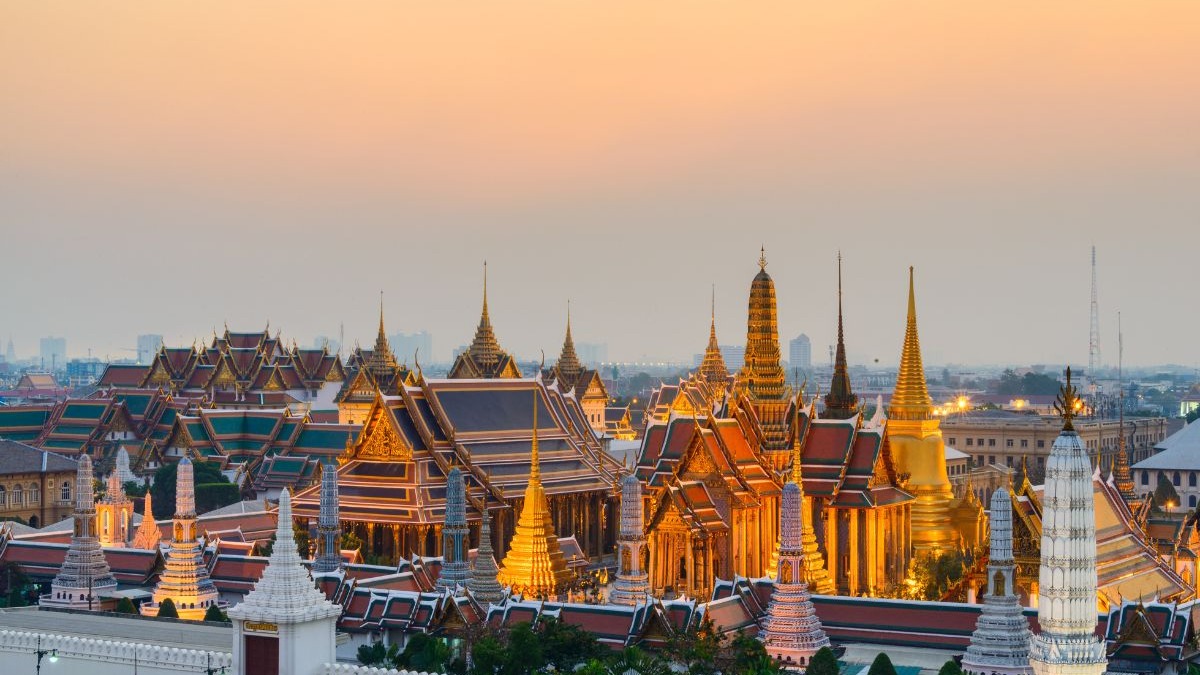 Complexo de templos tailandeses ornamentados, dourados e coloridos, iluminados ao anoitecer em Bangkok.
