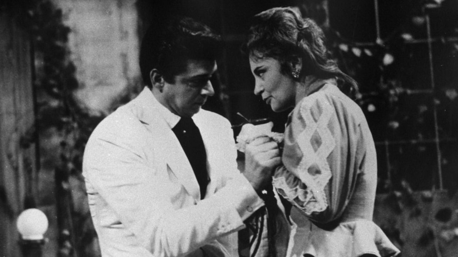 Close-up de um homem e uma mulher em cena dram&aacute;tica, m&atilde;os unidas, em preto e branco