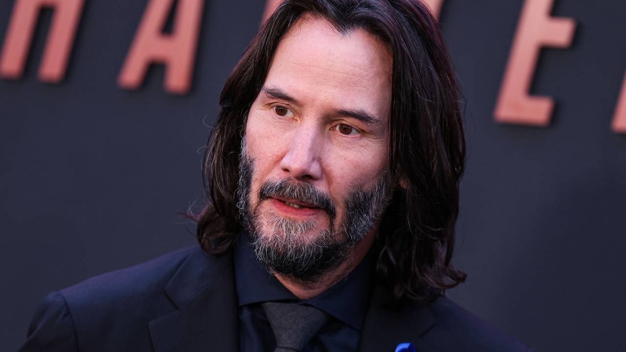 Keanu Reeves, que recusou atuar em uma sequência de sucesso, é um dos exemplos destacados na matéria. Close-up de Keanu Reeves, cabelo e barba longos, vestindo terno escuro e gravata