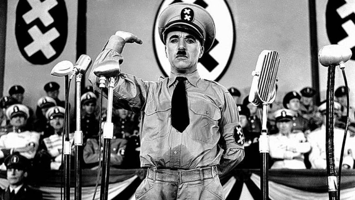 Charlie Chaplin como ditador caricato, com bigode e uniforme, bra&ccedil;o erguido, em um p&uacute;lpito com microfones.