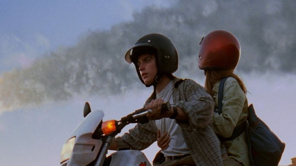 A luta pela sobrevivência e a desintegração social são motes de filmes sobre catástrofes cósmicas. Jovem homem e mulher de capacetes em motocicleta, com céu nublado e cinzento ao fundo