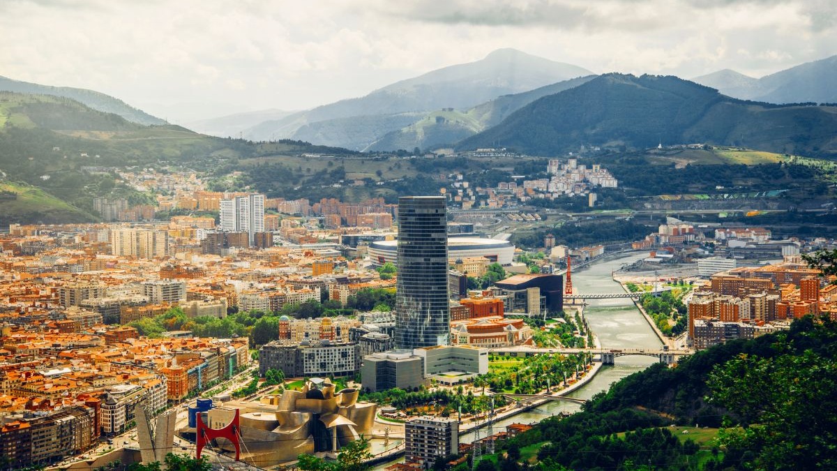 Vista panor&acirc;mica da cidade de Bilbao com rio, edif&iacute;cios, Guggenheim e montanhas ao fundo.