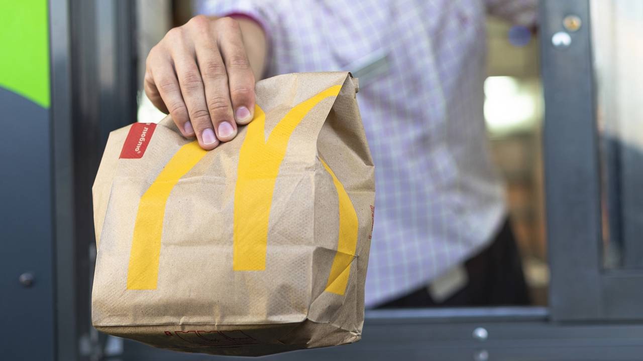 O molho especial é um dos segredos mais bem guardados que torna o lanche do McDonald's inconfundível, agora com versão caseira. Mão segura sacola de papel McDonald's marrom com logo amarelo e adesivo vermelho escrito 'Mobigo'