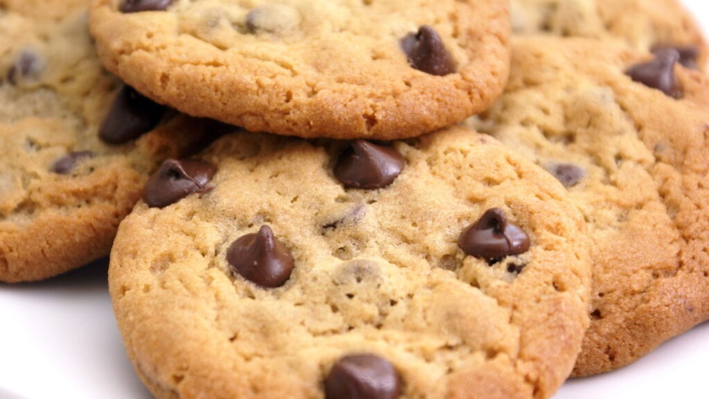 Cookies com a textura ideal, crocantes por fora e macios por dentro, dependem de um preparo correto. Cookies de chocolate chip dourados, alguns sobrepostos, com gotas de chocolate aparentes