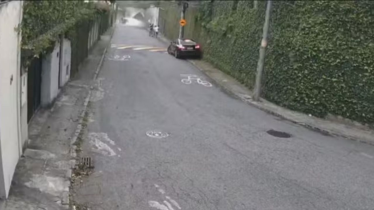 Queda de muro mata duas pessoas durante ventania em Santa Teresa. Rua inclinada, muro verde com carro estacionado e pessoas no fundo da via