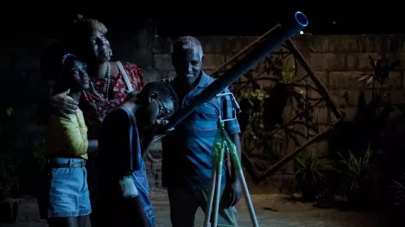 Uma família de quatro pessoas observa o céu com um telescópio em um quintal noturno