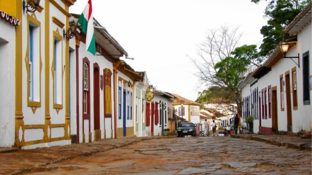 Rua de pedra em Ouro Preto, com casarões coloniais coloridos e pessoas caminhando ao fundo.