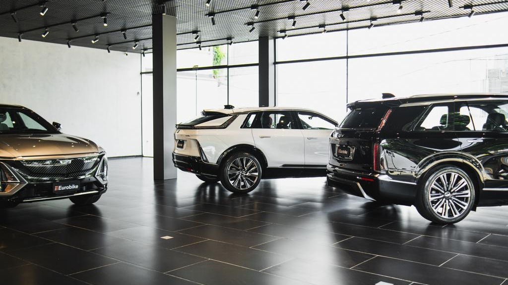 Tr&ecirc;s SUVs de luxo em showroom da Eurobike, incluindo modelos el&eacute;tricos Cadillac, com logo vis&iacute;vel
