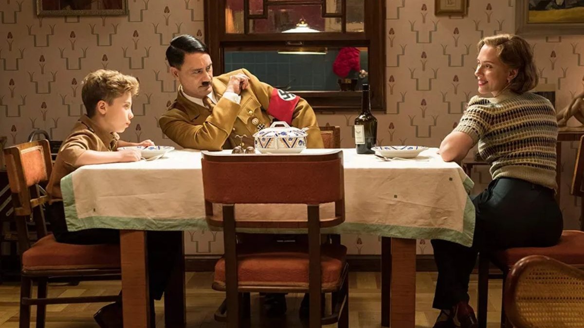 Tr&ecirc;s pessoas, um menino, um homem como Hitler e uma mulher, &agrave; mesa de jantar.