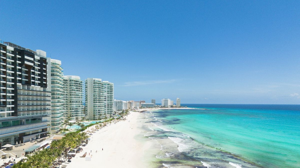 Vista panor&acirc;mica de praia com areia branca, mar azul-turquesa e arranha-c&eacute;us hoteleiros em Canc&uacute;n.