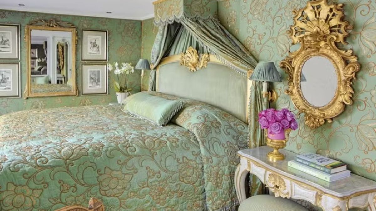Quarto de luxo com cama dossel verde e dourada, espelho ornamentado e papel de parede floral.
