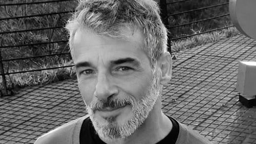 Retrato em preto e branco de Carlos Cesare, homem com cabelo e barba grisalhos olhando &agrave; frente