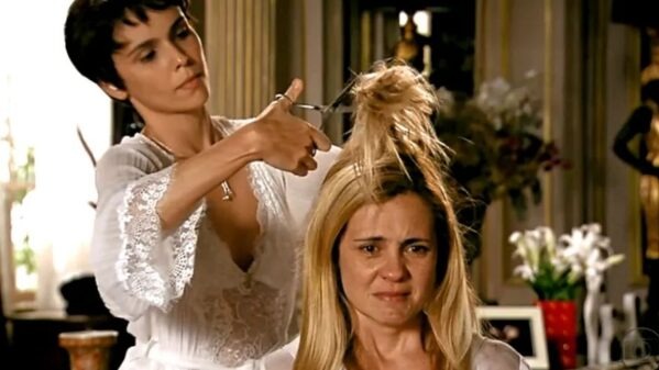 O retorno de Carminha e Nina em 'Avenida Brasil 2' remete a cenas marcantes da novela original. Foto: Reprodução Mulher de cabelo escuro com tesoura corta o cabelo loiro e bagunçado de mulher chorando