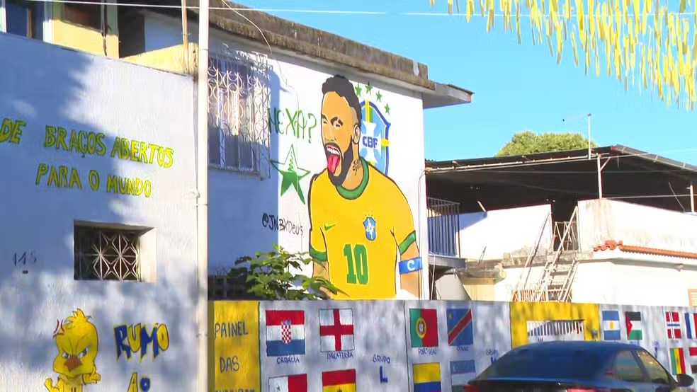 Mural de Neymar e bandeiras de países decoram a Rua Taturana, vencedora do concurso de ornamentação para a Copa do Mundo. Mural de Neymar com camisa do Brasil e bandeiras de países em muro decorado de rua.