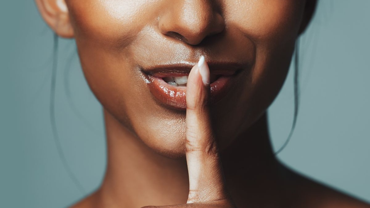 Close-up de mulher com o dedo indicador sobre os lábios, em gesto de silêncio.