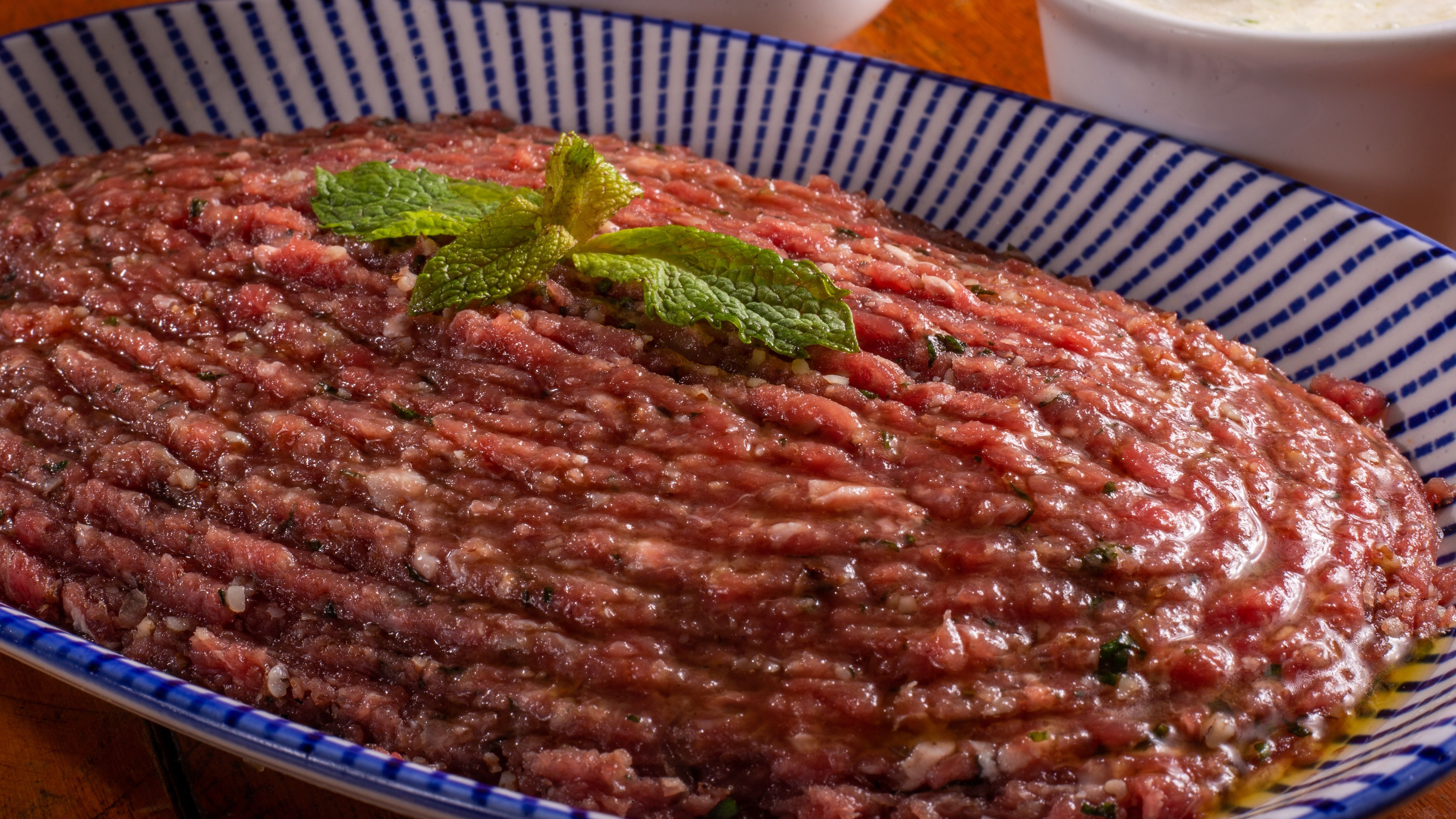A carne de onça, iguaria curitibana à base de carne moída crua, é um dos pratos típicos da culinária paranaense. Carne moída crua temperada com folhas de hortelã frescas em um prato azul e branco.