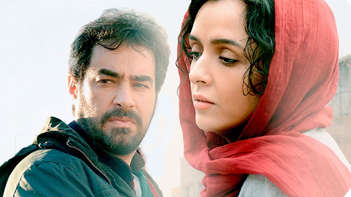 Close-up de homem barbudo com jaqueta e mulher de len&ccedil;o vermelho, ambos com semblante s&eacute;rio.