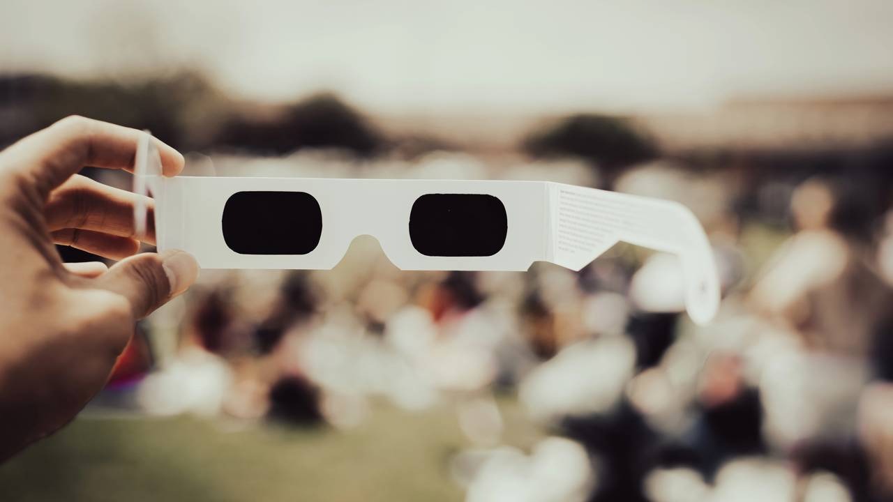 Óculos especiais com filtros são essenciais para a observação segura do eclipse solar de 2026, protegendo a visão do Sol. Mão segura óculos brancos de papelão com lentes escuras para eclipse