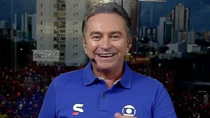 Rembrandt Júnior, que retorna à Globo para narrar em Pernambuco e no Sportv, em registro durante transmissão. Foto: Reprodução Homem sorridente de camisa polo azul da Globo e Sportv com headset, frente a cidade