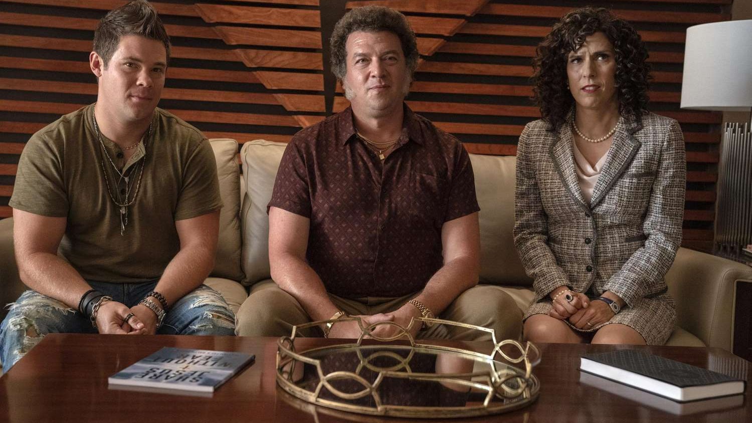 Três pessoas sentadas em sofá: dois homens e uma mulher. Todos olham para frente.