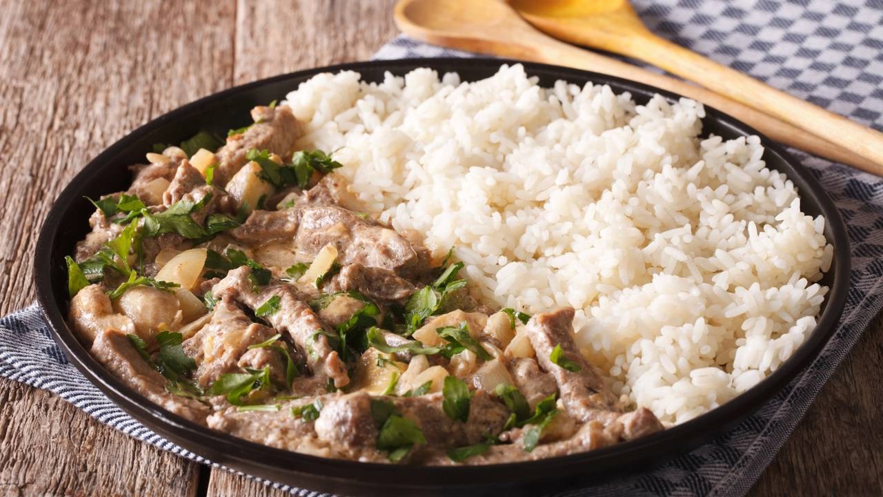 O clássico strogonoff, como o da receita light de frango, é uma opção reconfortante e prática para as refeições do dia a dia. Prato com strogonoff de carne, arroz branco e salsinha, sobre mesa de madeira
