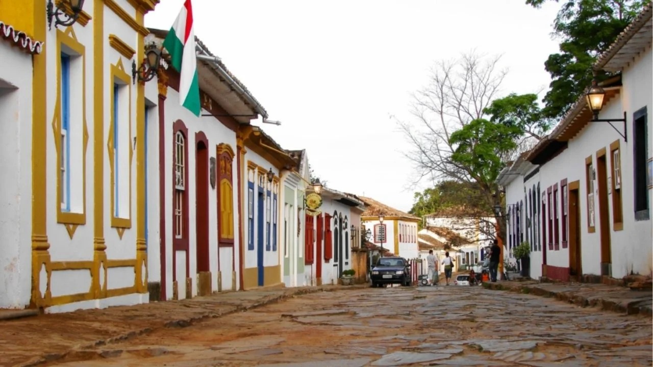 Ruas de pedra e casarões coloniais preservam o charme histórico de Tiradentes, um dos destinos que encantam Minas Gerais. Rua de pedra em Tiradentes com casarões coloniais coloridos, poste de luz e pessoas.