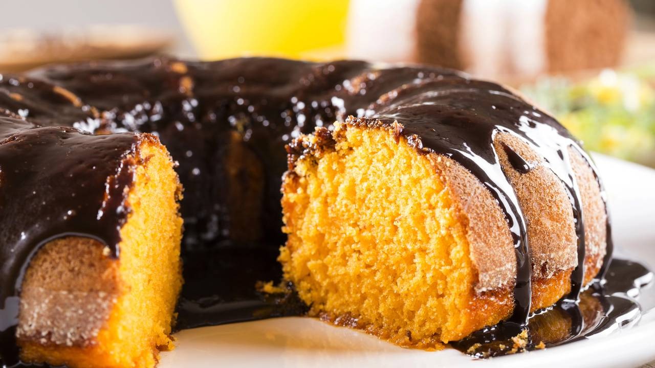 Bolo de cenoura com cobertura de chocolate escorrendo e fatia cortada revelando massa fofa