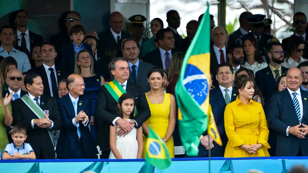 Jair Bolsonaro, Michelle Bolsonaro e a filha Laura em evento p&uacute;blico com bandeiras do Brasil