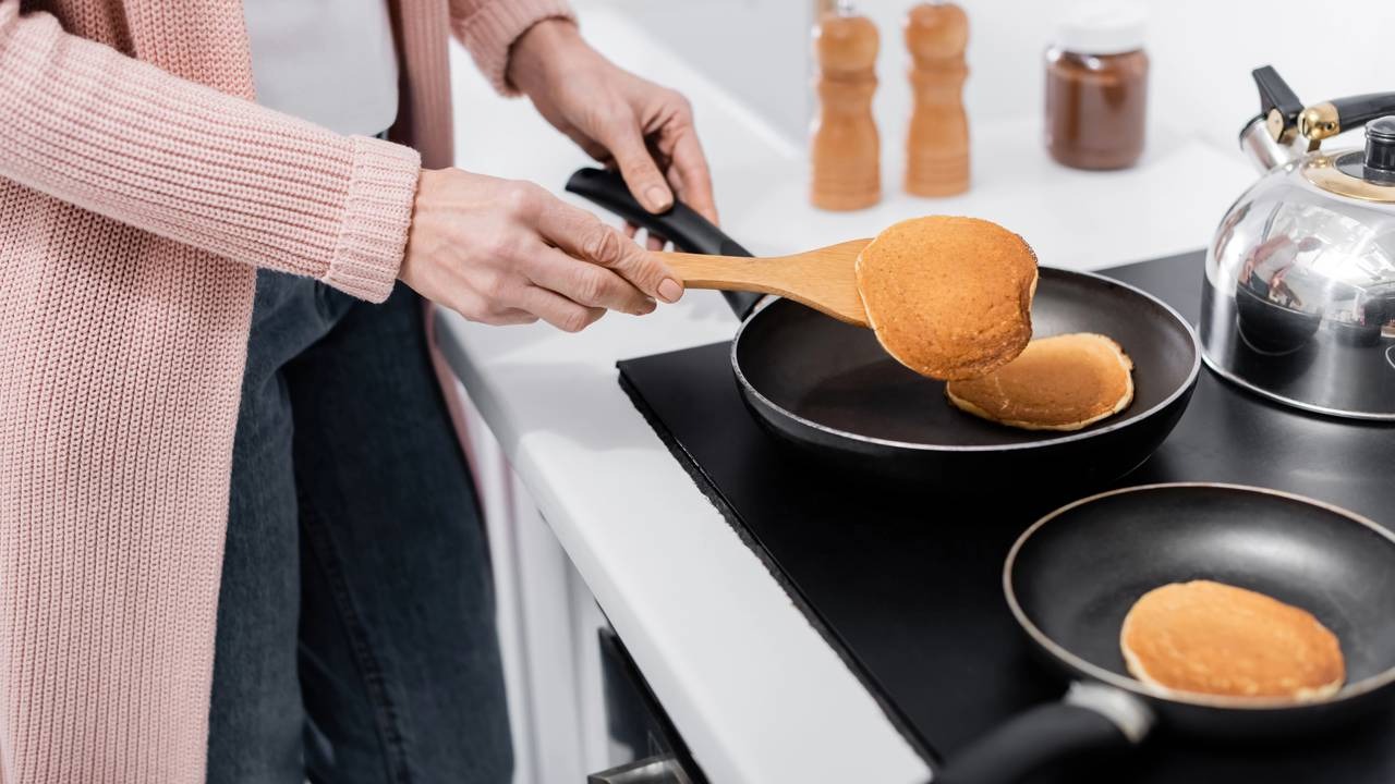 Siga o modo de preparo para dourar suas panquecas americanas na frigideira e ter um café da manhã delicioso. Pessoa virando panqueca em frigideira com espátula de madeira na cozinha