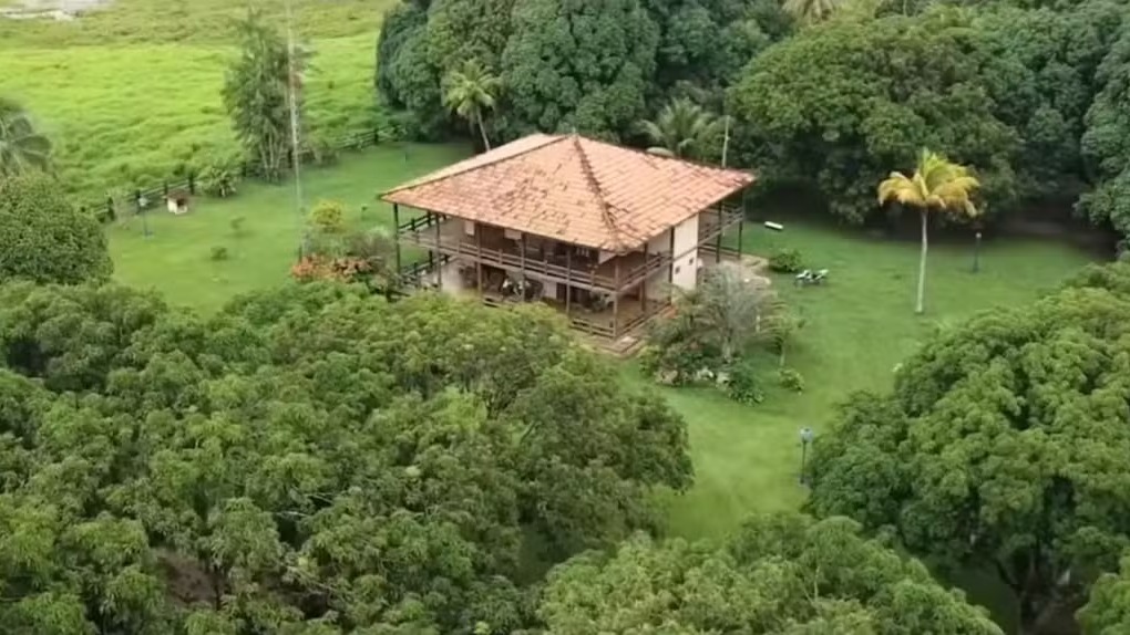 Vista aérea de casarão rural com telhado de telha, rodeado por árvores e gramado