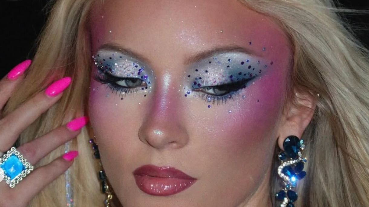 Close-up de mulher com maquiagem de glitter nos olhos, blush rosa, l&aacute;bios brilhantes e unhas pink.