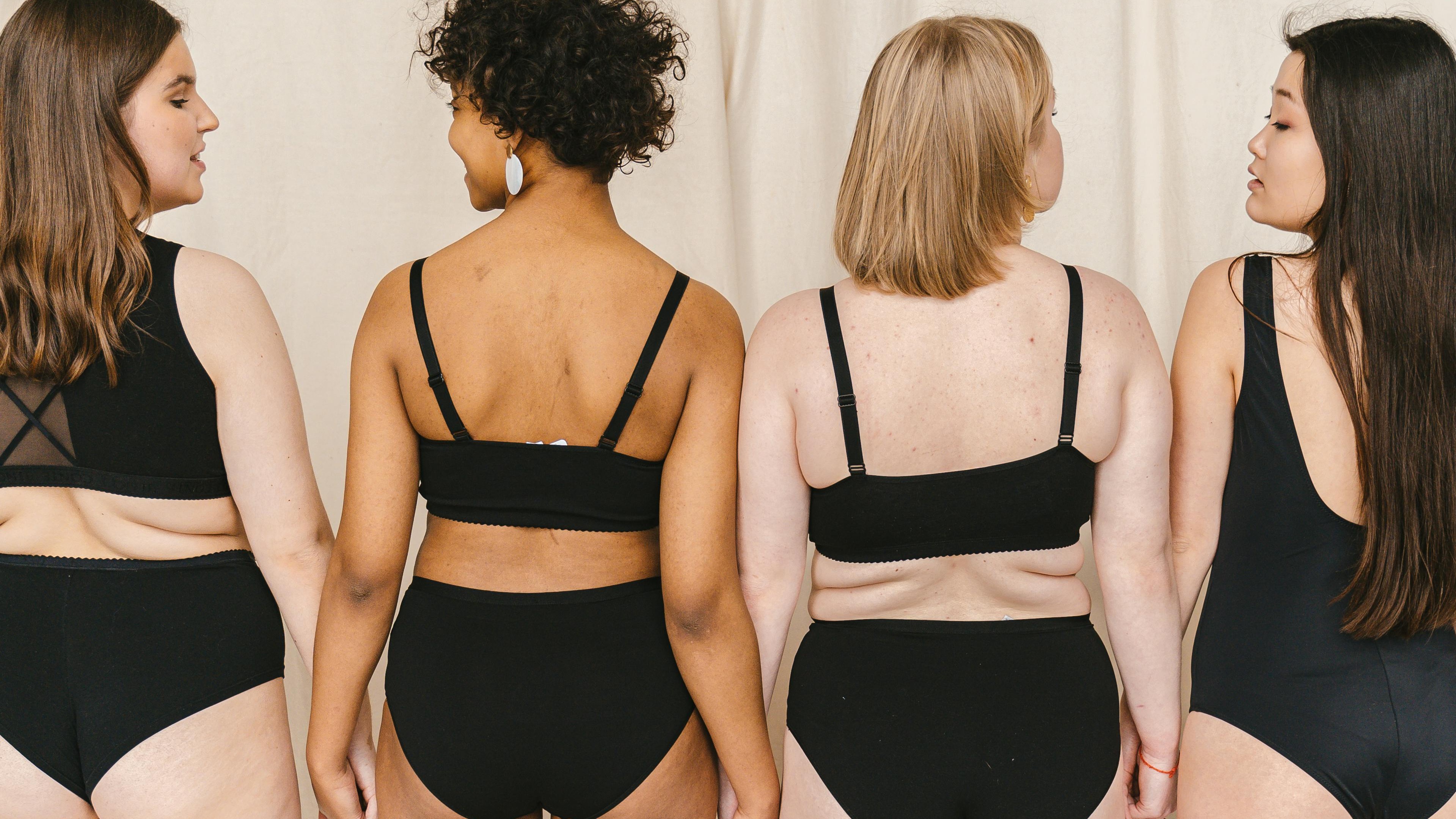 Quatro mulheres com diferentes tons de pele e corpos, de costas, usando suti&atilde; e calcinha pretos.