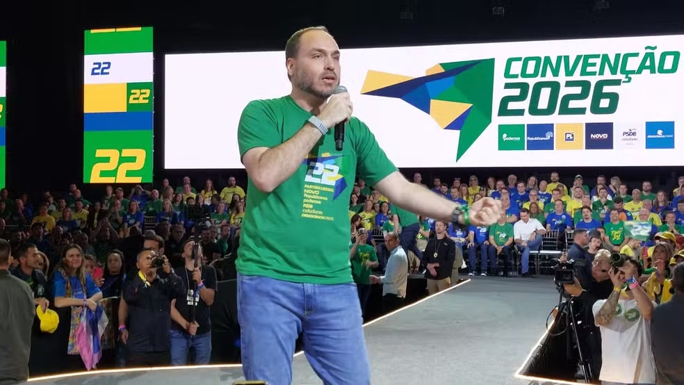 Homem discursa no palco, camiseta verde, microfone. Telas: 'Conven&ccedil;&atilde;o 2026', '22', logos partid&aacute;rios.