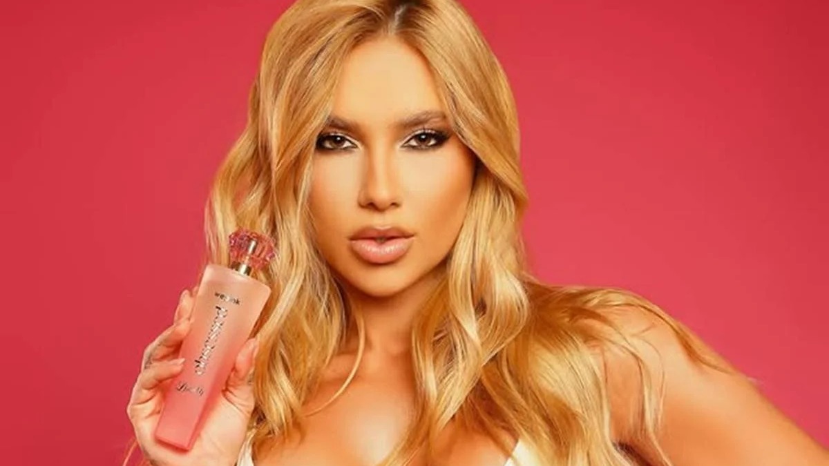 Produto WePink: a linha de cosméticos da influenciadora Virginia Fonseca que movimenta bilhões no mercado brasileiro. Mulher loira segura frasco de perfume rosa WePink Obsessed contra fundo rosa