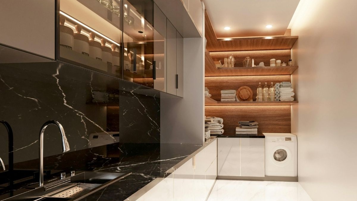 Cozinha moderna com bancada de m&aacute;rmore preto, pia, arm&aacute;rios superiores e prateleiras iluminadas com m&aacute;quina de lavar.