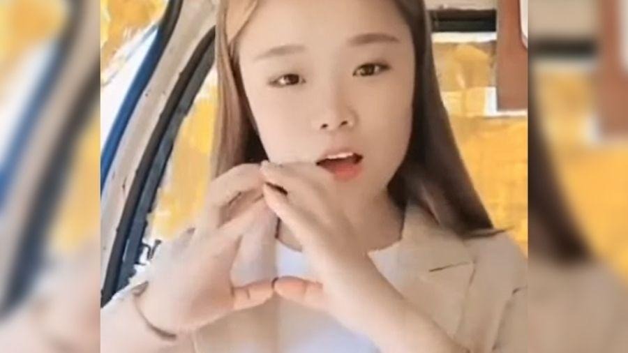 A influenciadora chinesa Xiao Qiumei, que morreu em uma live perigosa, é um dos exemplos trágicos da busca por conteúdo viral. Jovem mulher asiática com cabelo comprido fazendo um gesto com as mãos e a boca aberta.