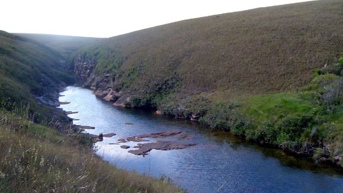 Rio sinuoso em vale verdejante com encostas gramadas e rochas aparentes.