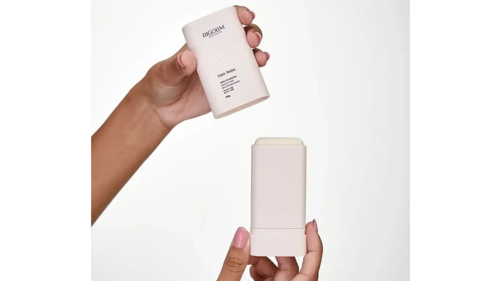 M&atilde;os de mulher seguram dois bast&otilde;es de cera Rigolim Hair Balm, um aberto, em fundo branco