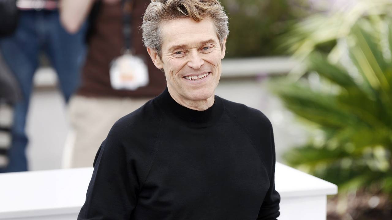 Willem Dafoe, aclamado por “O Homem que Vendeu sua Sombra”, foi surpreendentemente esnobado pela Academia no Oscar 2026. Willem Dafoe em close-up, sorrindo, com cabelo grisalho e suéter preto de gola alta.